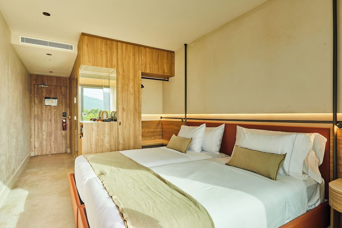 A modern hotel room with a large bed, wooden panel walls, and a view of the outdoors.