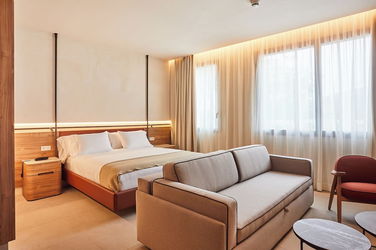 A modern hotel room with a bed, a sofa, a chair, and a small table.