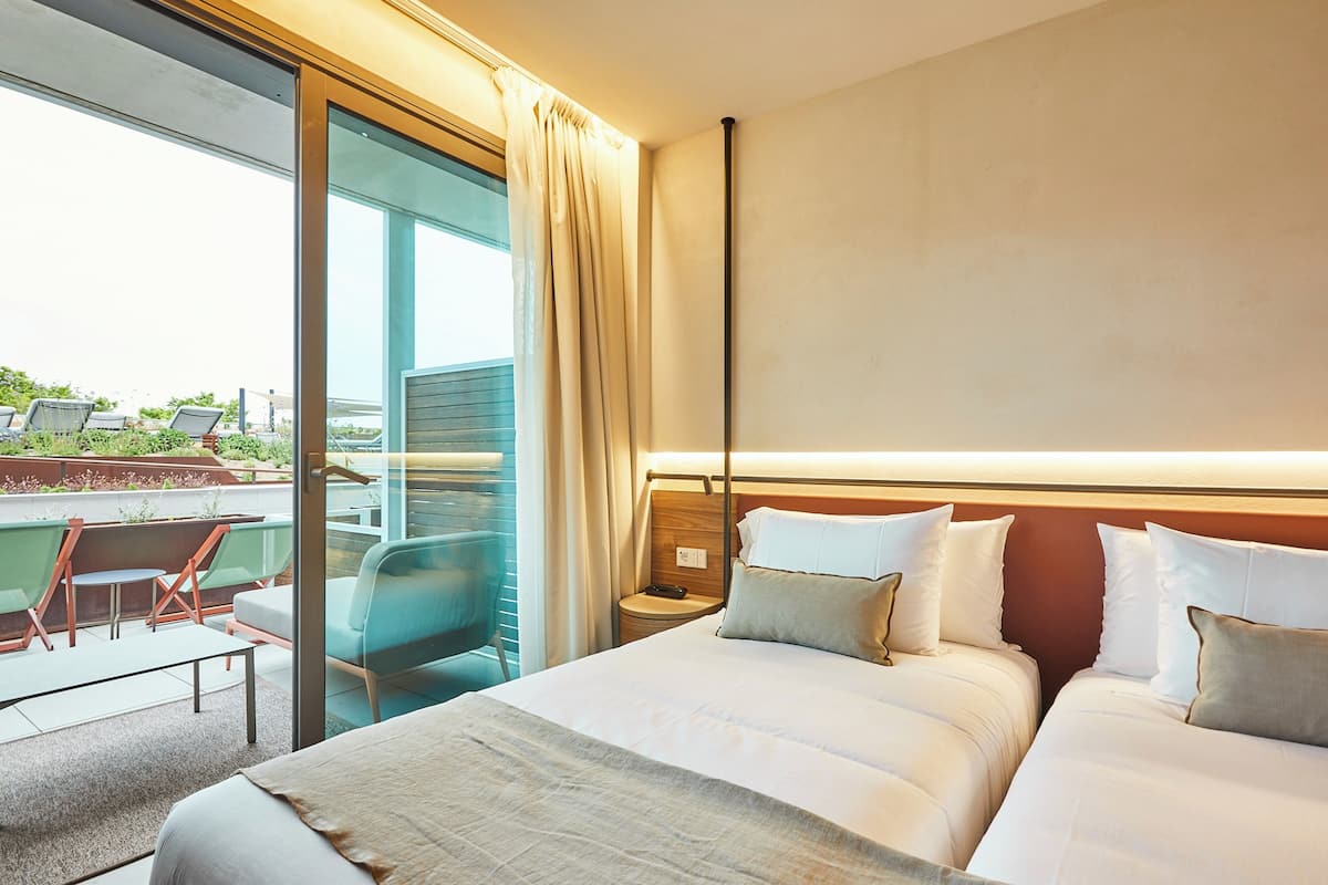 A hotel room with a large bed, a bedside table, a chair, and a view of the outdoors.