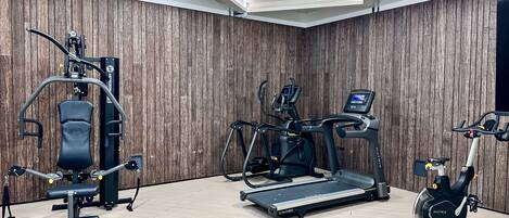 Une salle de sport équipée d’un tapis de course, d’un vélo elliptique et d’appareils de musculation.