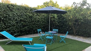 A patio area with a blue lawn, a table with chairs, and a large umbrella. - Maison Entièrement Clôturée à 2mn en Voiture de la Plage (Saint-Florent)