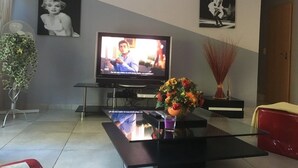 A living room with a flat-screen TV, a glass coffee table, and two framed pictures on the wall. - Maison Entièrement Clôturée à 2mn en Voiture de la Plage (Saint-Florent)
