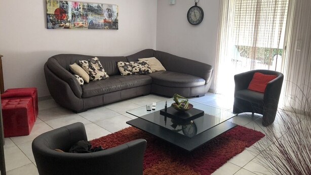 A living room with a sectional sofa, a coffee table, a red ottoman, and a chair with a red cushion. - Maison Entièrement Clôturée à 2mn en Voiture de la Plage (Saint-Florent)