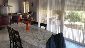 A dining area with a marble table, chairs, a vase with flowers, and a view through large windows. - Maison Entièrement Clôturée à 2mn en Voiture de la Plage (Saint-Florent)