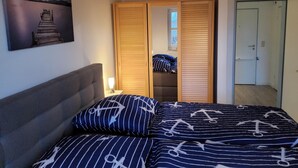 A bedroom with a bed, a wooden wardrobe, a painting, and a nightstand with a lamp. - Apartment Seebrücke Schönberger Strand, bright and friendly, dog is welcome (Schönberg)