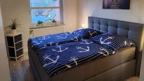 A bedroom with a bed, a window, a radiator, a plant, and a painting on the wall. - Apartment Seebrücke Schönberger Strand, bright and friendly, dog is welcome (Schönberg)