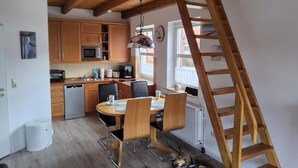 A modern kitchen with wooden cabinets, a dining table with chairs, a ladder, and a dog. - Apartment Seebrücke Schönberger Strand, bright and friendly, dog is welcome (Schönberg)