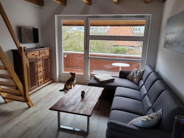 A modern living room with a wooden staircase, a grey sofa, a wooden coffee table, and a TV on the wall. - Seebrücke Schönberger Strand Apartment: Bright and Welcoming, Dogs Allowed (Schönberg)
