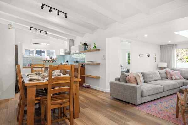 Una cocina moderna con zona de comedor, un sofá gris y suelo de madera.