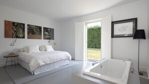 A modern bedroom with a large bed, a bathtub, and artwork on the walls. - Casa Briteiros - (Guimarães)