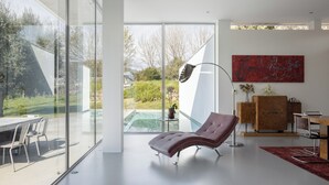 A modern interior with a glass wall, a lounge chair, a dining area, and a red abstract painting. - Casa Briteiros - (Guimarães)