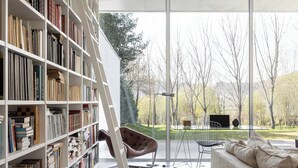 A modern living room with a large bookshelf, a leather chair, a glass table, and a sofa. - Casa Briteiros - (Guimarães)