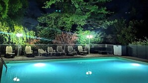 A swimming pool with lounge chairs and a fence, surrounded by trees and night lighting. - Gîte for 12 to 20 people with heated swimming pool, in Aveyron 🌿 (La Fouillade)