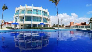 Un hotel moderno con una piscina grande, varios balcones y palmeras.