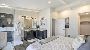 Un dormitorio moderno con una cama grande, cabina de ducha de vidrio, tocador con espejo y vestidor.