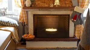 A cozy room with a fireplace, a bed with a checkered blanket, and a basket of oranges. - Dandy Villas Dimitsana a family home in a quaint historic neighborhood  (Dimitsana)