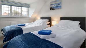 A hotel room with two beds, a window with blinds, a painting on the wall, and a lamp on the nightstand. - Crannog - Three Bedroom Cottage, Sleeps 6 (Llandudno)