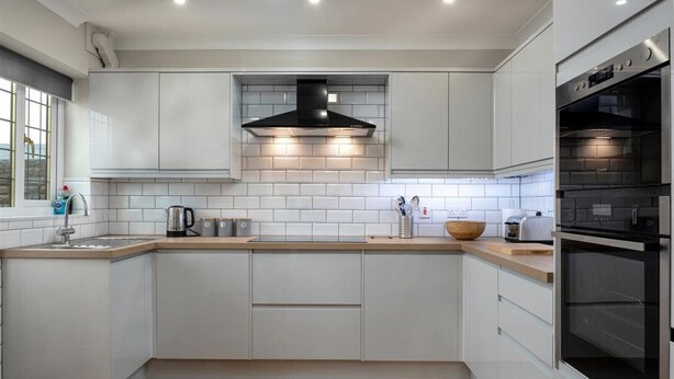 A modern kitchen with white cabinets, a black range hood, and a built-in oven. - Crannog - Three Bedroom Cottage, Sleeps 6 (Llandudno)