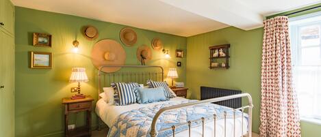 Un dormitorio con estructura de cama metálica, pared verde y ventana con cortinas estampadas.