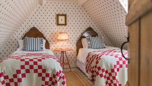 Ein gemütliches Zimmer mit zwei Betten, Wandtapete mit Muster, einem kleinen Tisch mit Lampe und einem gerahmten Bild an der Wand.