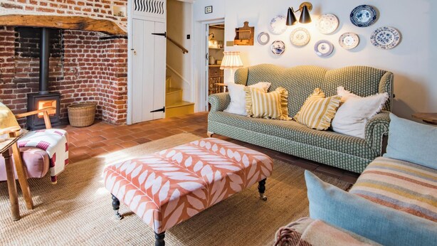 Ein gemütliches Wohnzimmer mit Kamin aus Backsteinen, einem gemusterten Sofa und einem Essbereich mit Tisch und Stühlen.