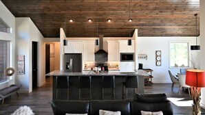 A modern kitchen with a central island, bar stools, and a dining area with a red lamp. - Mustang Mountain Retreat in Bison Ridge! (Show Low)