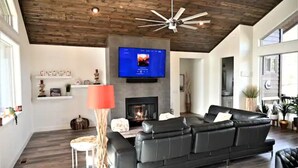 A modern living room with a fireplace, a black leather sofa, and a television mounted above it. - Mustang Mountain Retreat in Bison Ridge! (Show Low)