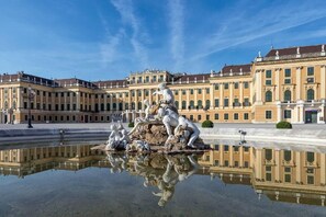 A classical fountain with sculptures in front of a large, ornate building with multiple windows and balconies.