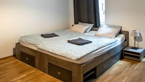 Une chambre à coucher moderne avec un cadre de lit en bois, une couvre-lit à motifs gris et blancs, et un rideau noir.