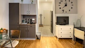 Une cuisine de taille réduite avec un coin repas, une horloge au mur et un téléviseur posé sur un meuble.