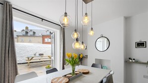 A modern dining area with a table set for four, a vase of yellow flowers, and hanging light fixtures. - 4 Bedroom Seaside House, Beach 220m with Free Parking (Sidmouth)