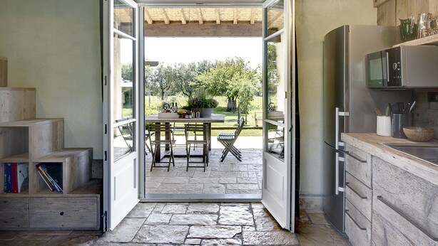 Une cuisine avec une porte ouverte donnant sur un patio aménagé avec une table et des chaises.