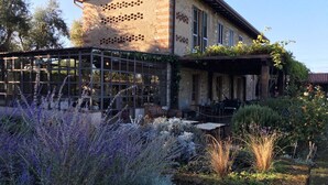 Un bâtiment rustique doté d’une structure en verre, entouré d’un jardin où poussent de la lavande et d’autres plantes.