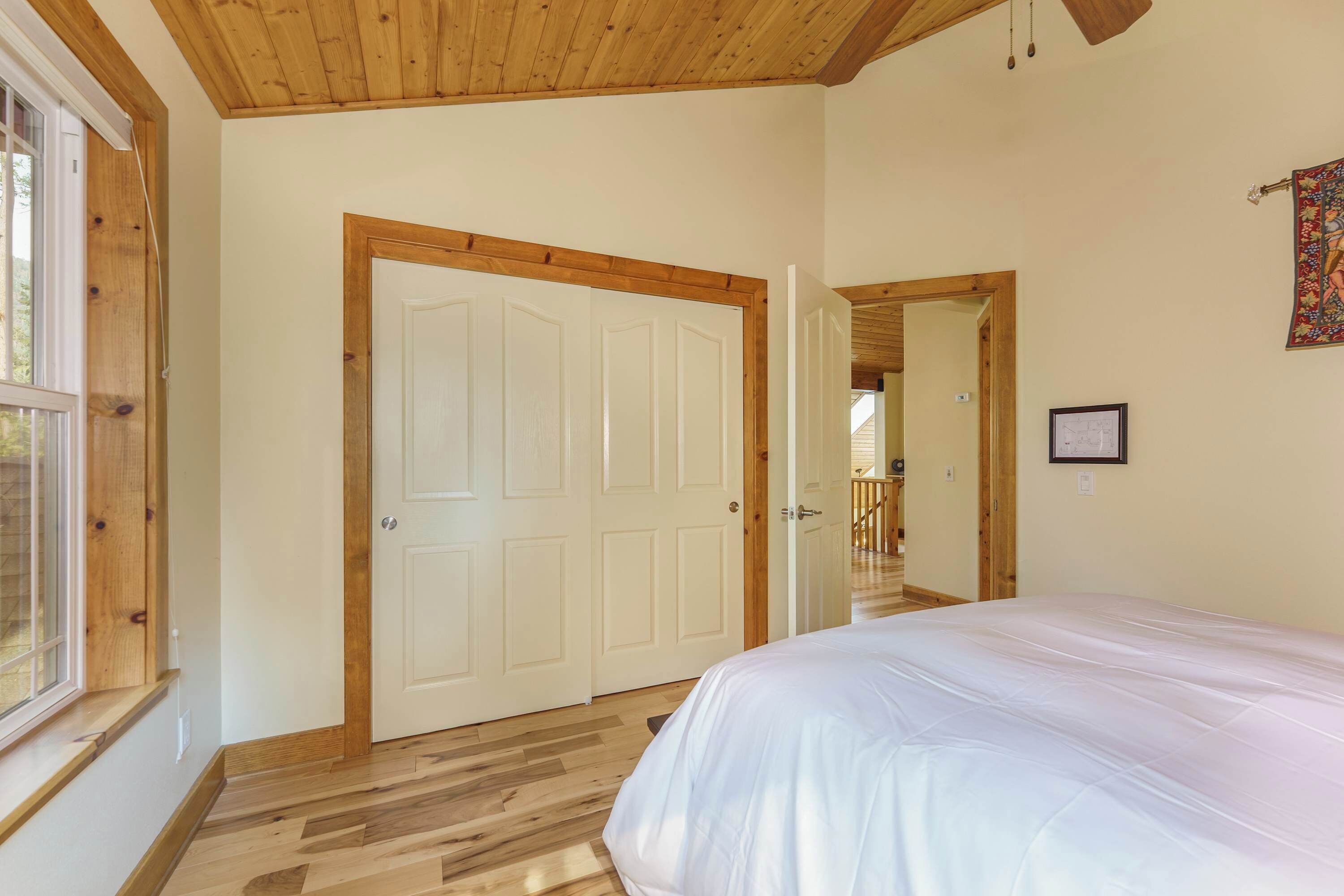 A bedroom with a wooden floor, a white bed, and a door leading to another room.