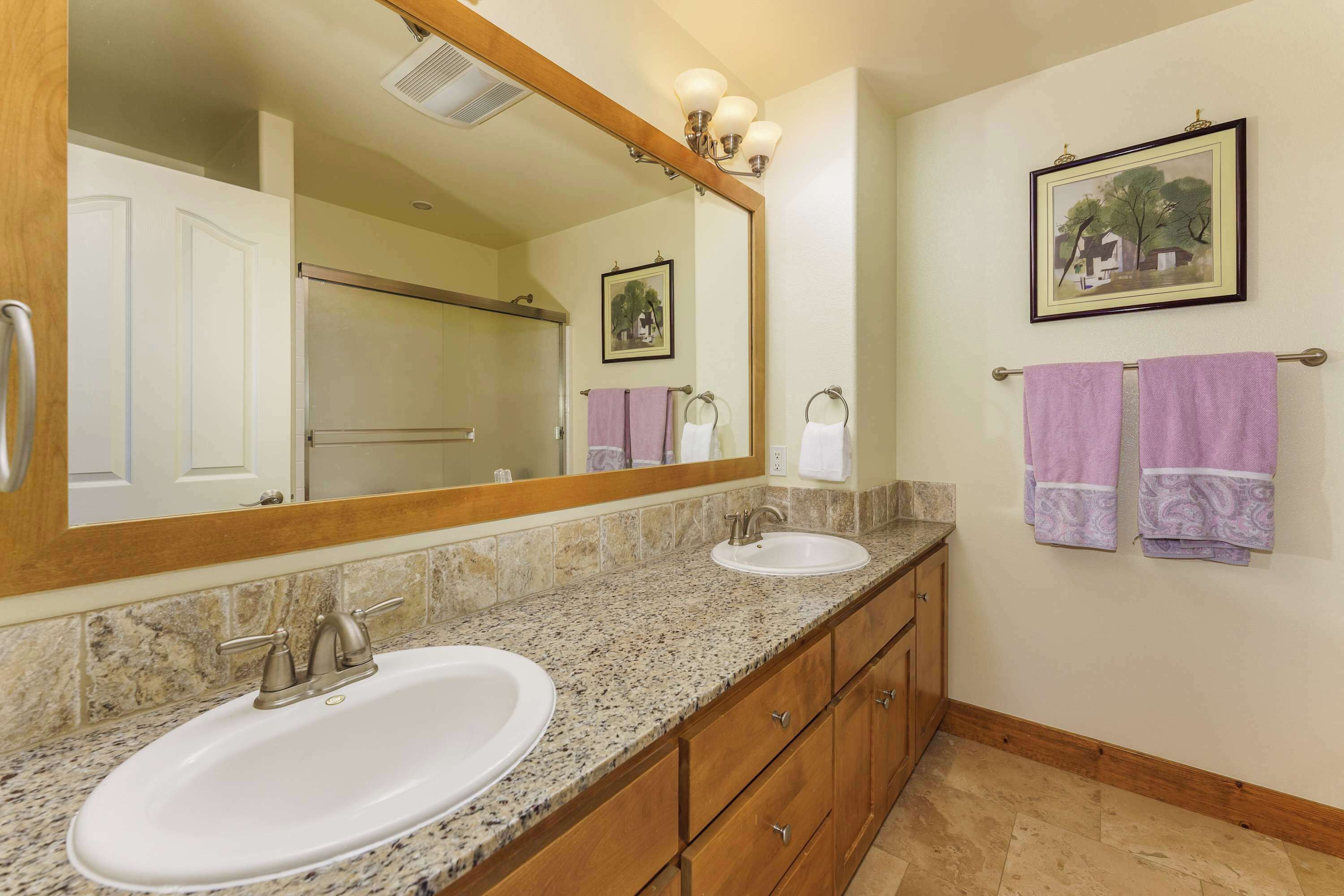 A bathroom with two sinks, a large mirror, wooden cabinets, and two towels hanging on a towel rack.