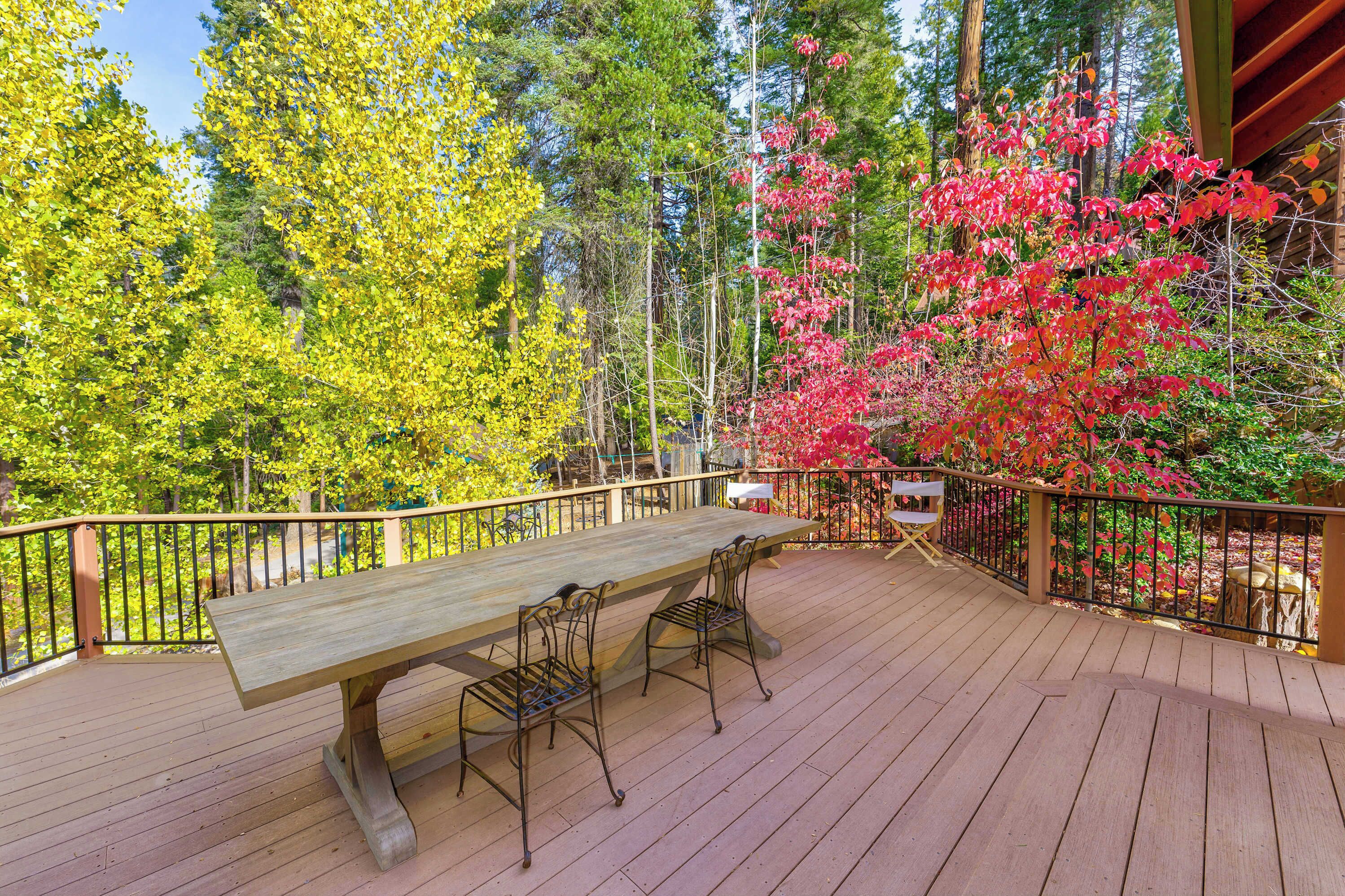 A wooden deck with a table and chairs, surrounded by trees and a metal railing.