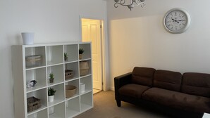 Ein Wohnzimmer mit einer weißen Regaleinheit, einem braunen Sofa, einer Deckenleuchte und einer Wanduhr.