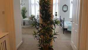 Ein Flur mit einem Blumentopf, der zu einem Essbereich mit Tisch und Stühlen sowie zu einem Schlafzimmer mit Bett und Kommode führt.