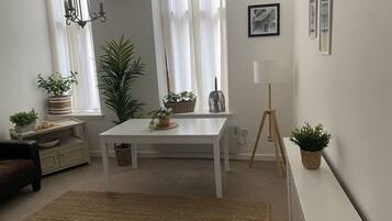 Uma sala de estar moderna com uma mesa branca, um sofá, um abajur e várias plantas.