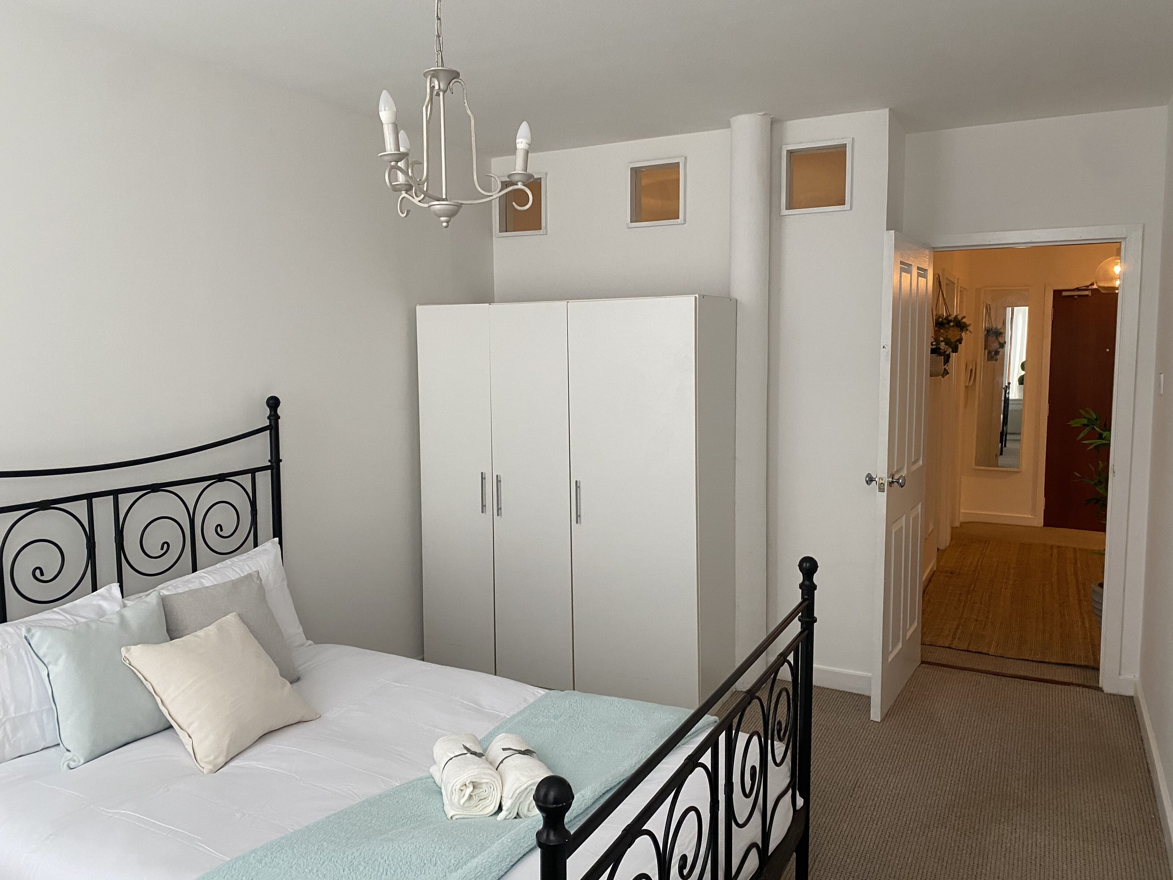 A bedroom with a bed, a wardrobe, a chandelier, and a door leading to another room.