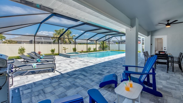 Patio esterno con piscina, sedie a sdraio, barbecue e zona salotto coperta.