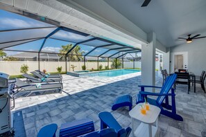 An outdoor patio with a pool, lounge chairs, a grill, and a covered seating area. - Villa Sparkle Blue - renovated with large pool and spa (Cape Coral)
