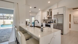 Una cucina moderna con una grande isola, elettrodomestici in acciaio inossidabile e vista su una piscina.