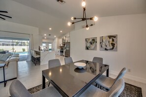 Una cocina moderna con armarios blancos, un refrigerador de acero inoxidable y una zona de comedor con mesa de vidrio y sillas grises.