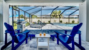 Patio esterno con poltrone Adirondack blu, un barbecue e una piscina.
