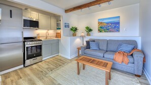 A modern kitchen with stainless steel appliances, a grey sofa, and a painting of a landscape. - 108MT #3: Stunning 1BDR + Views, BBQ + Harbor Views + Golf Cart (Avalon)