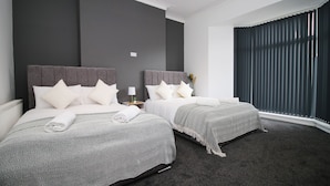 A hotel room with two beds, dark walls, and a large window with blinds.