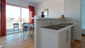 A compact kitchen with a sink, a dining area with chairs, and a view through a sliding glass door to an outdoor balcony. - France - Appt pour 4 proche plage (Benodet)
