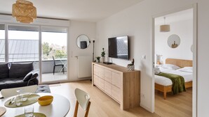 A modern, well-lit room with a sofa, dining table, and a bed. - Le Rochenoire - Appt proche plage (Dinard)