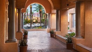 Un pasillo con columnas, plantas en macetas y vistas a mesas al aire libre.